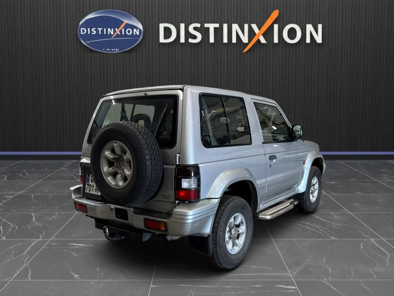 Vue 3/4 arrière droite du Mitsubishi Pajero Court gris aluminium de 1997 avec roue de secours et marchepieds visibles.