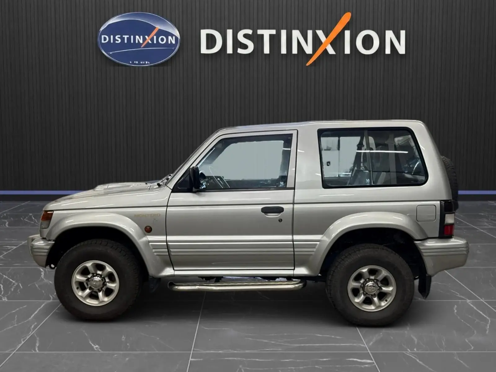Profil droit du Mitsubishi Pajero Court gris aluminium de 1997 avec marchepieds et jantes alliage 15 pouces.