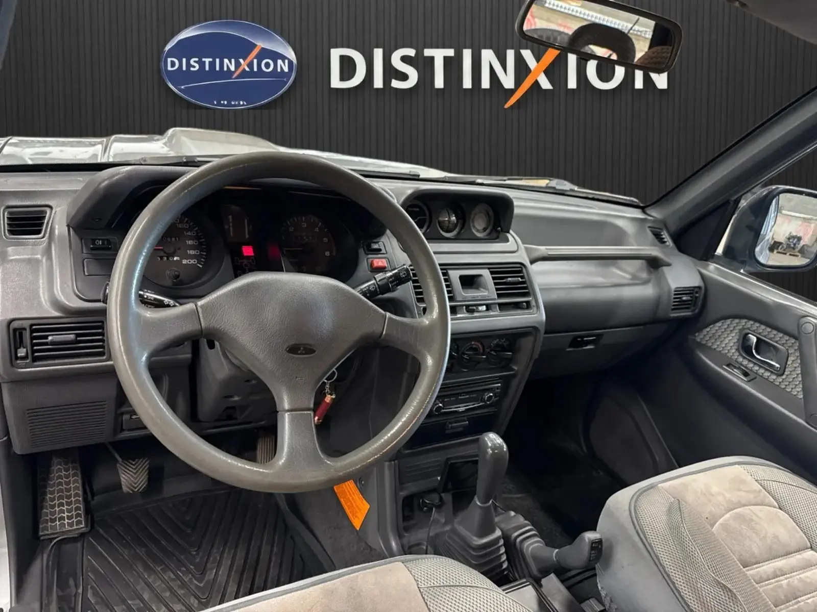 Intérieur gris du Mitsubishi Pajero Court 2.8 TD 1997, vue du poste de conduite avec volant et levier de vitesses manuel.