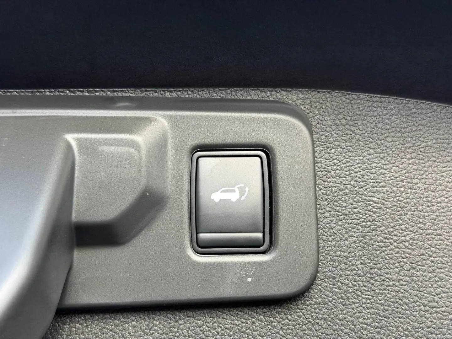 Bouton d'ouverture électrique du coffre sur panneau intérieur en plastique gris d'un Renault Austral noir étoilé.