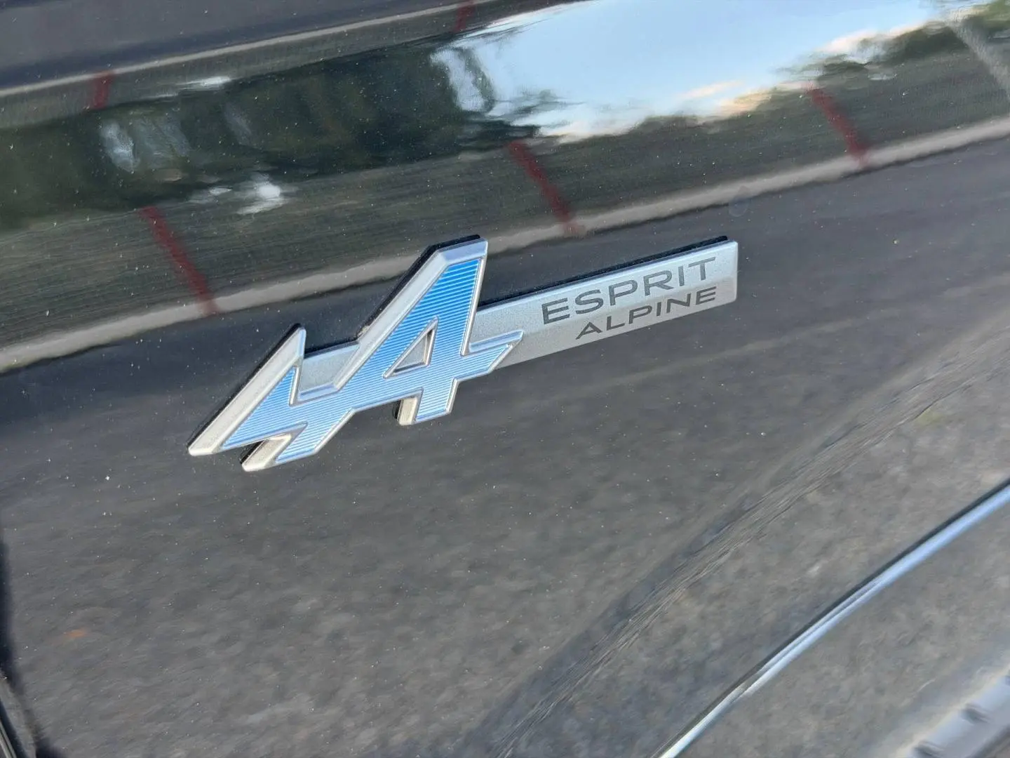 Gros plan sur l’inscription Esprit Alpine bleue sur la carrosserie noir étoilé métallisé du Renault Austral.
