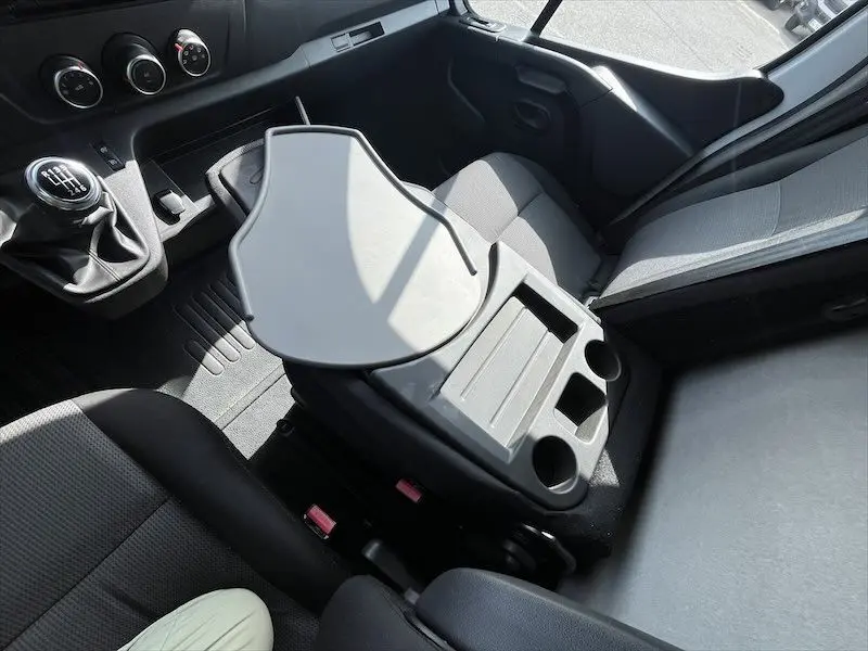 Intérieur du Renault Master blanc 2021, vue plongeante sur la console centrale avec tablette rabattable et sièges gris.