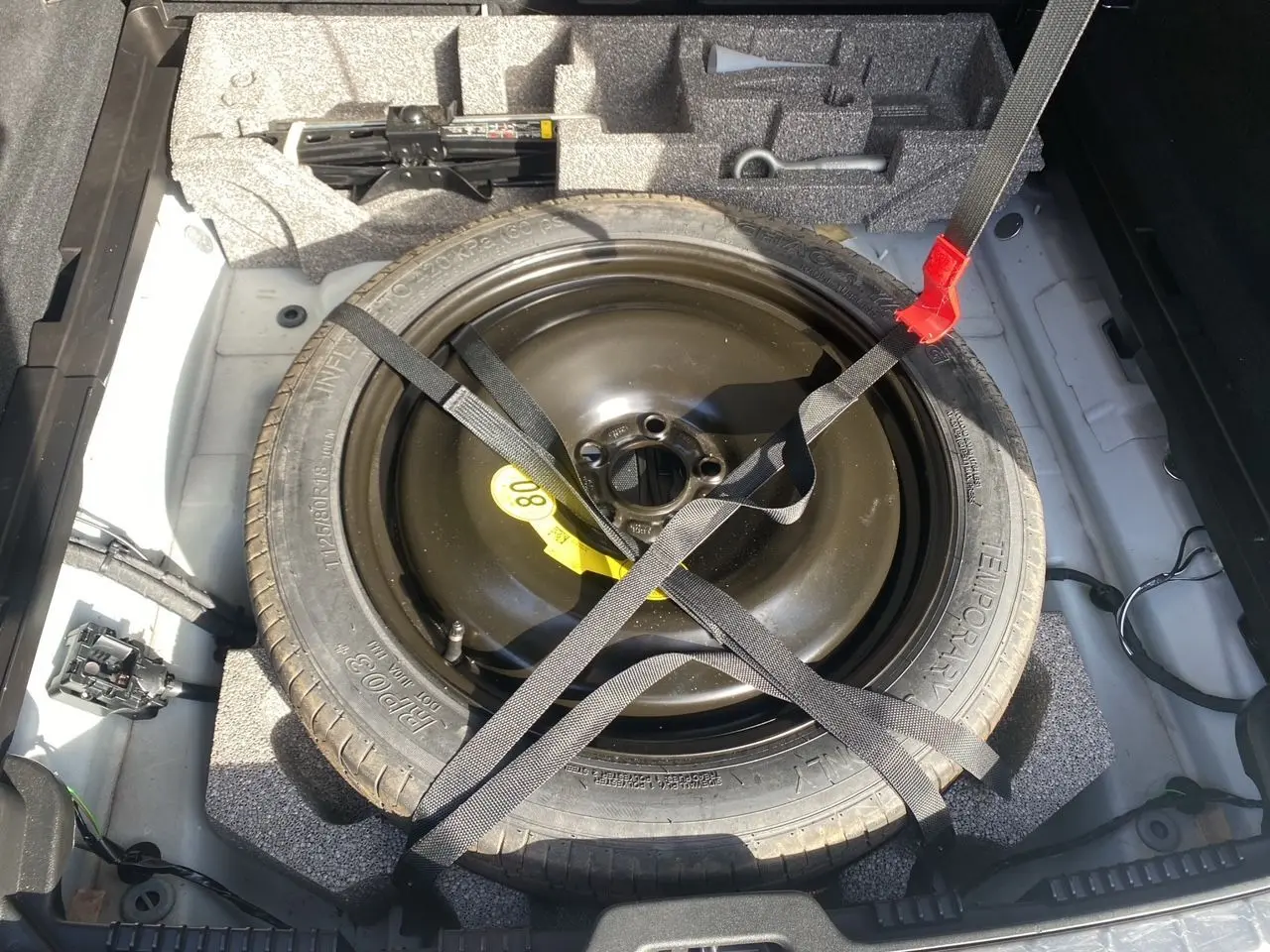 Roue de secours noire attachée par des sangles dans le coffre d'un Volvo XC60 blanc 2019, vue de dessus.