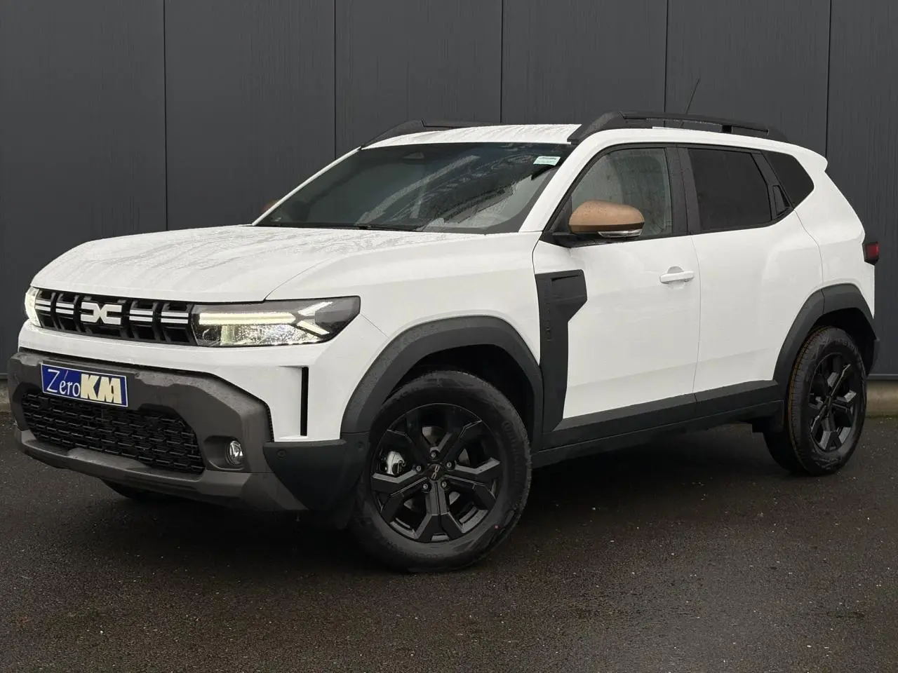 Vue 3/4 avant droite du Dacia Duster blanc Glacier avec coques de rétroviseurs brun cuivré et jantes noires.