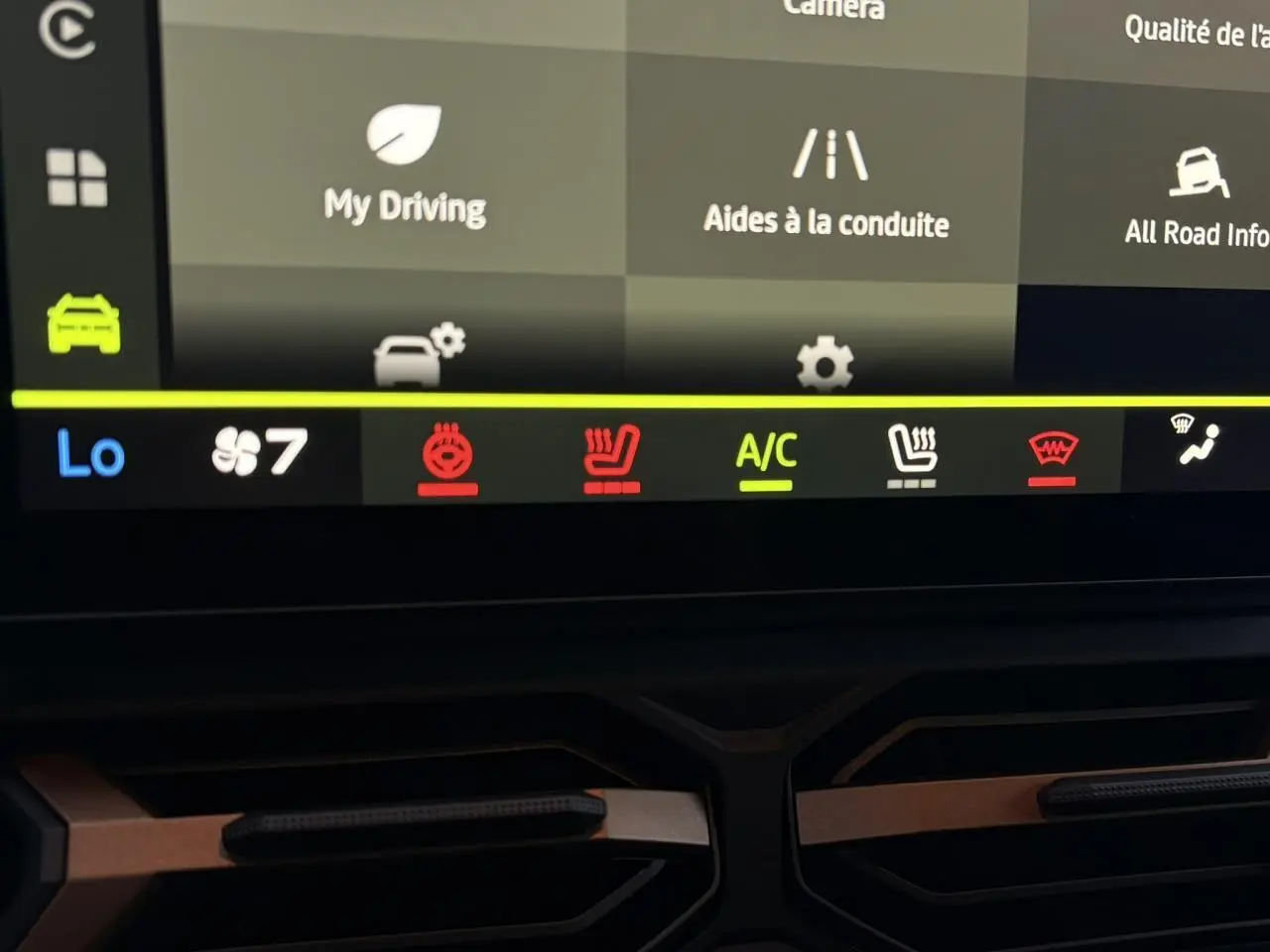 Détail de l’écran tactile du tableau de bord du Dacia Duster blanc, affichant les commandes de climatisation et aides à la conduite.