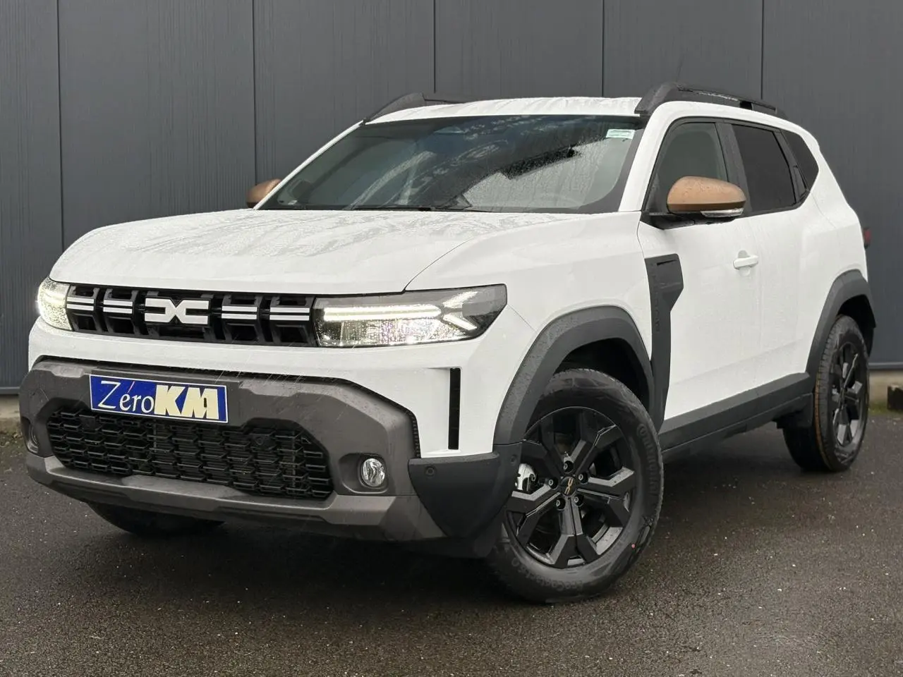 Dacia Duster blanc glacier en 3/4 avant droit, avec coques de rétroviseur brun cuivré et jantes noires.