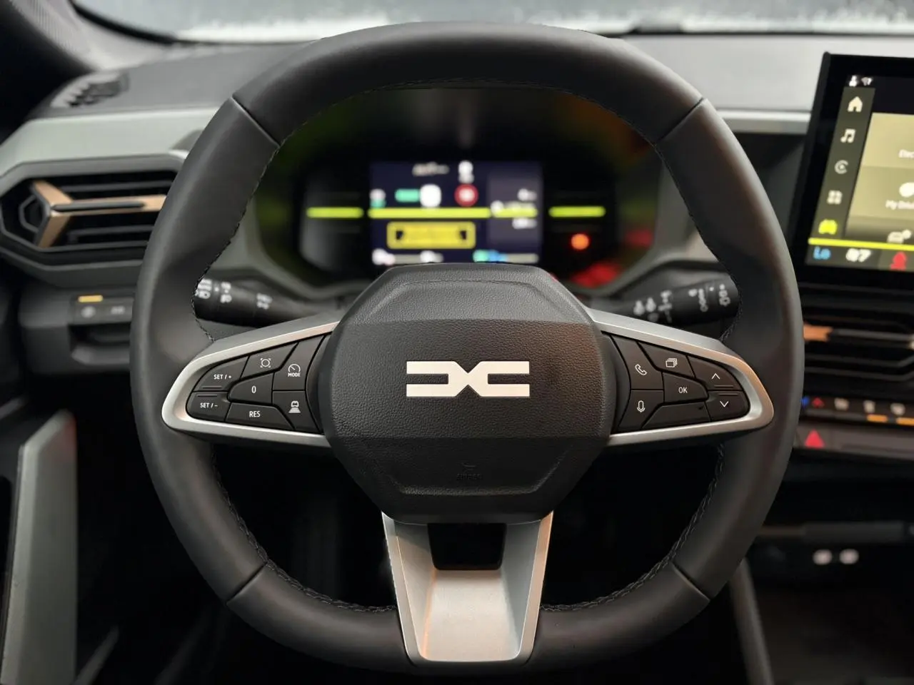 Vue rapprochée du volant noir du Dacia Duster 2026 avec commandes intégrées et tableau de bord digital en arrière-plan.