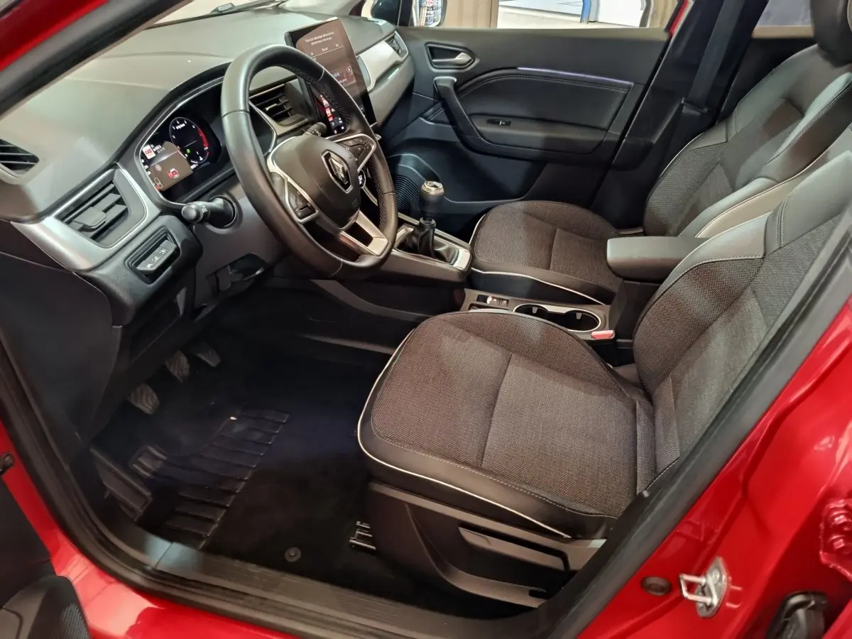 Intérieur avant droit du Renault Captur rouge 2024, volant multifonctions, sièges tissu gris et levier de vitesses manuel visible.