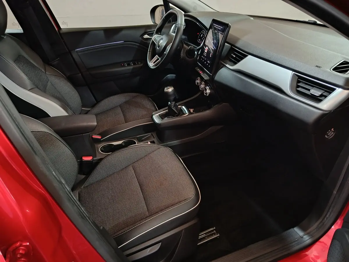 Intérieur avant droit du Renault Captur rouge 2024, avec tableau de bord moderne et écran tactile vertical.