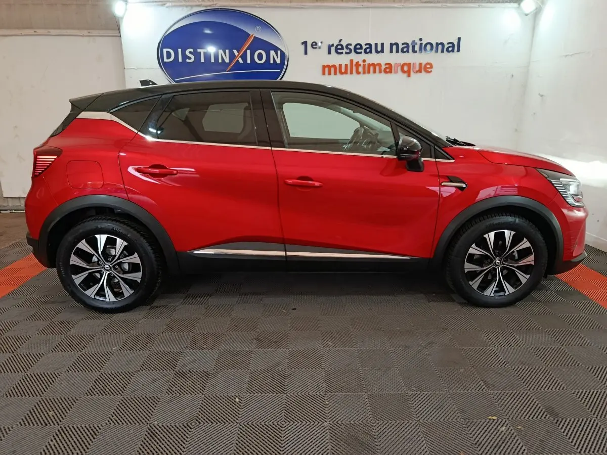 Profil droit d'un Renault Captur rouge 2024 avec jantes noires et toit noir, stationné en intérieur showroom.