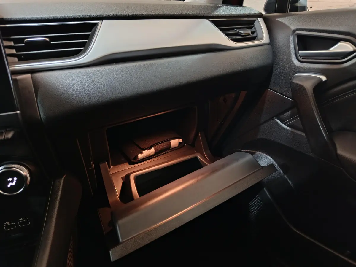 Intérieur noir du Renault Captur 2024, vue côté passager sur la boîte à gants ouverte avec manuel visible.