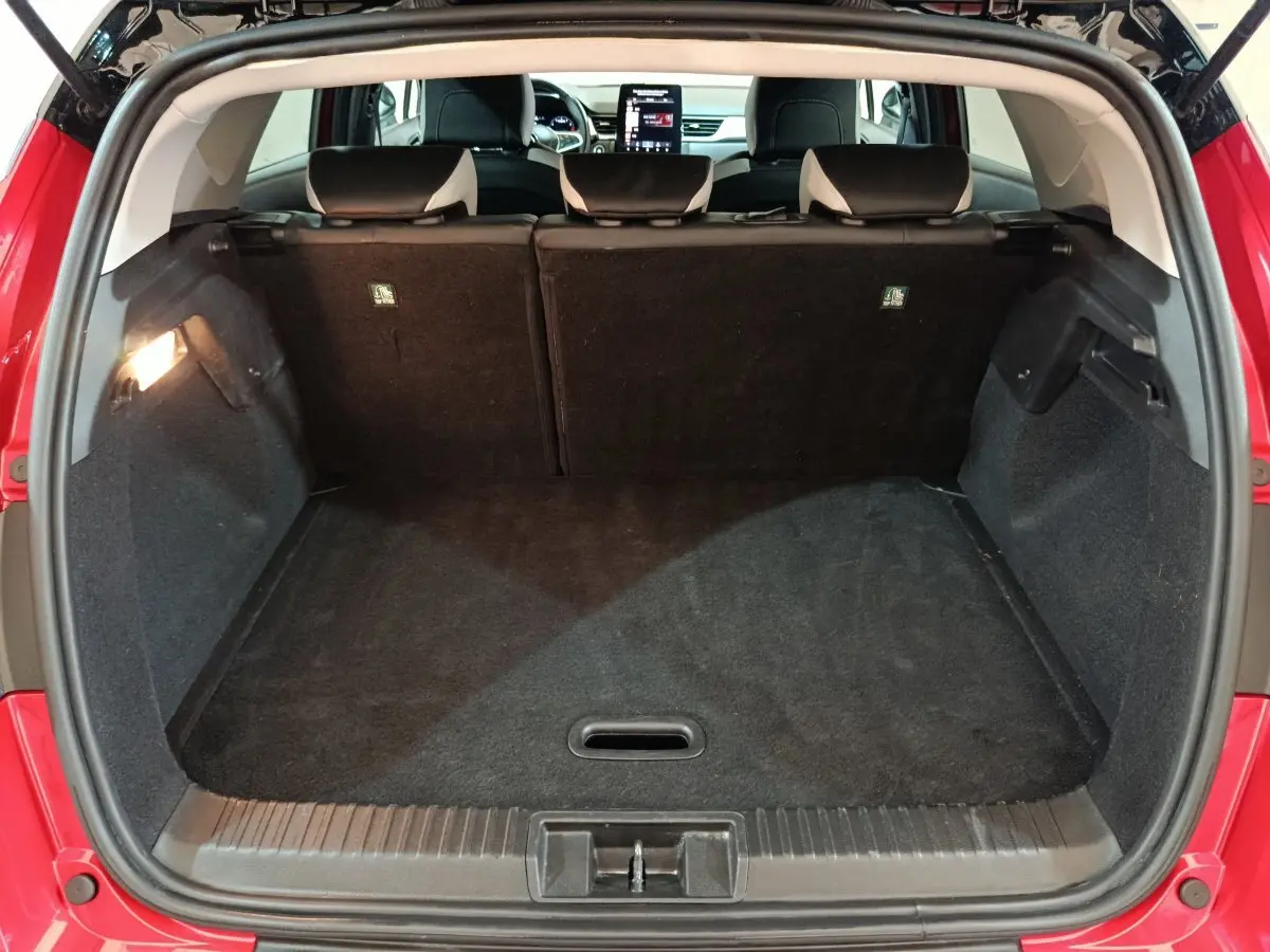 Coffre ouvert vu de l'arrière d'un Renault Captur rouge 2024, banquette arrière et écran tactile visibles à l'avant.