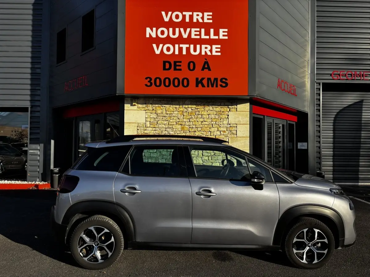 Profil côté gauche d'un Citroën C3 Aircross gris clair 2024 avec jantes alliage et barres de toit noires.