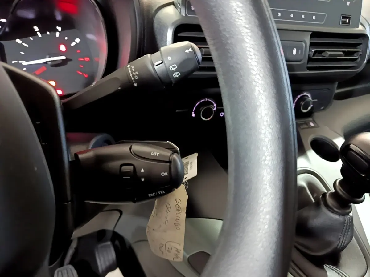Vue rapprochée de l'intérieur du Citroën Berlingo blanc, montrant le volant, levier de vitesses manuel et commandes au volant.