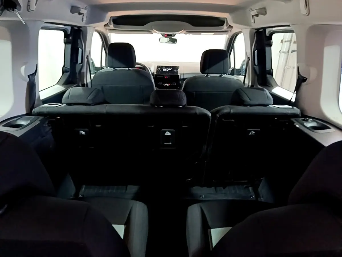 Vue intérieure arrière du Citroën Berlingo XL blanc, montrant les sièges noirs et le tableau de bord à l'avant.