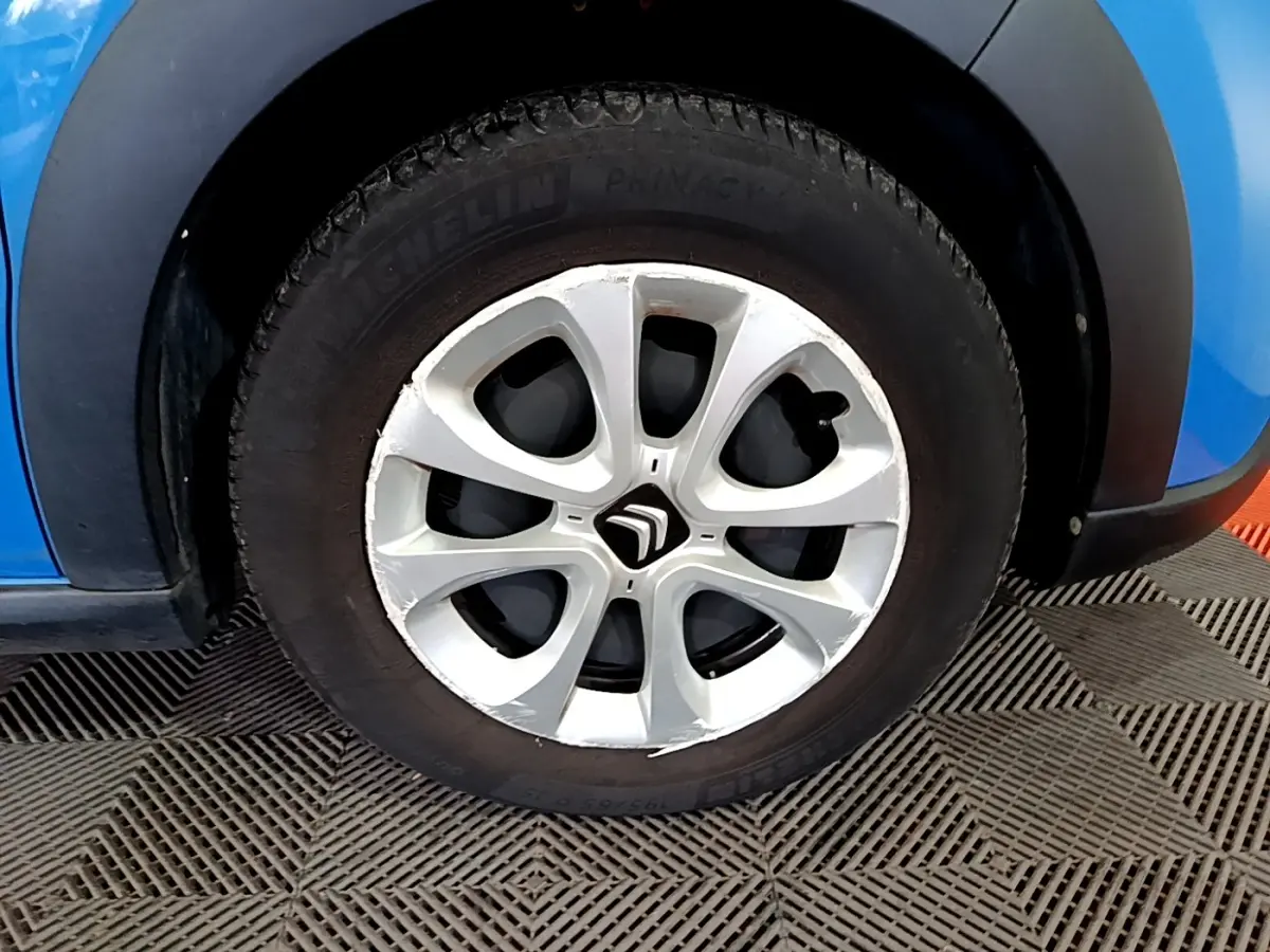 Gros plan sur la roue avant droite d'une Citroën C3 bleu, avec jante alliage et logo Citroën visible.