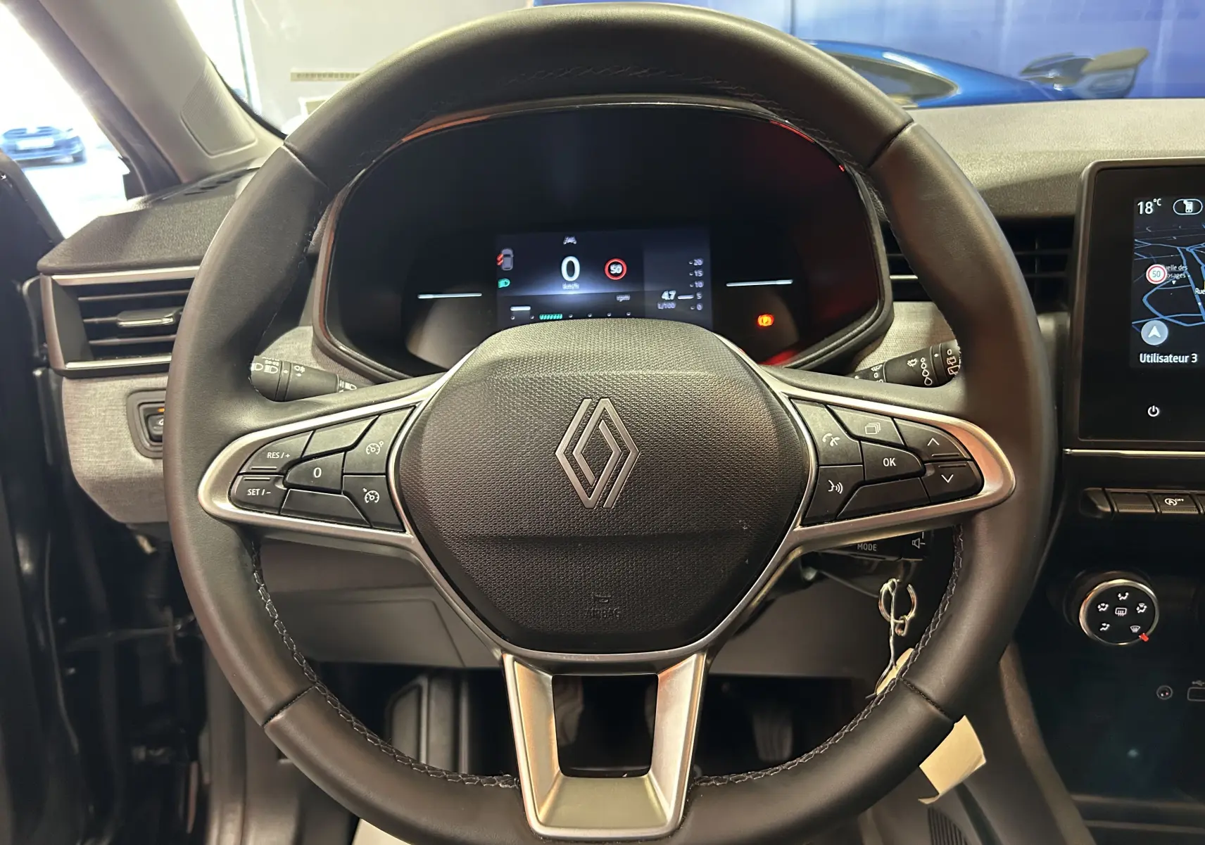 Vue intérieure centrée sur le volant noir de la Renault Clio V avec tableau de bord numérique et écran GPS à droite.