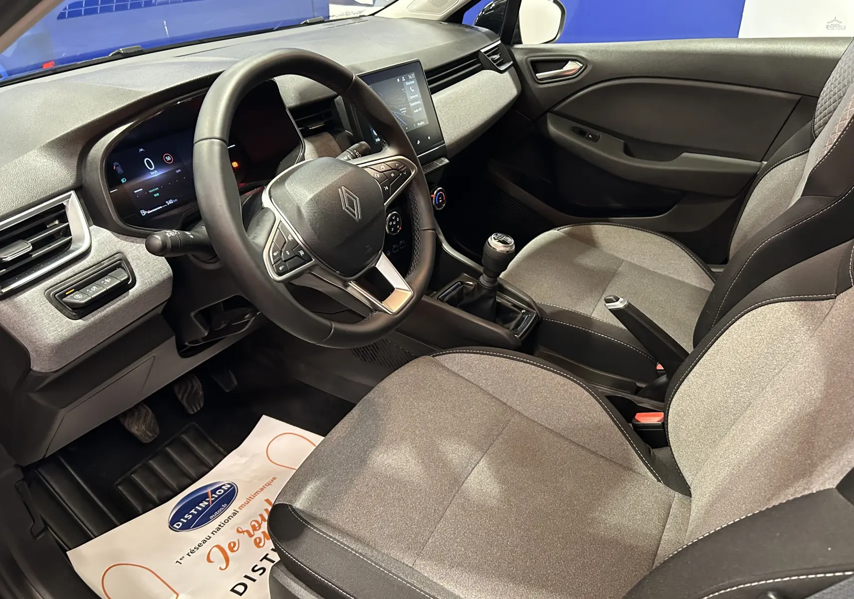 Intérieur avant droit de la Renault Clio V noire, montrant le volant, la console centrale avec boîte manuelle et les sièges tissu gris.
