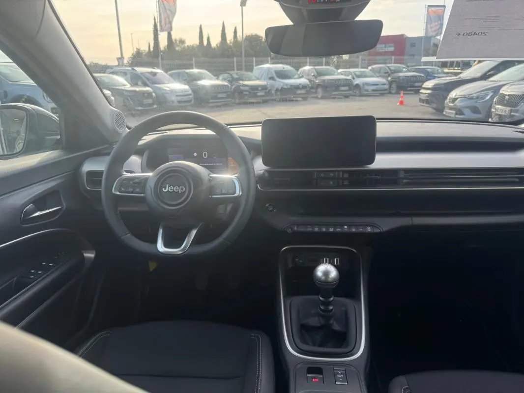 Vue intérieure frontale du Jeep Avenger gris 2025, avec volant multifonction, écran central et levier de vitesse manuel.