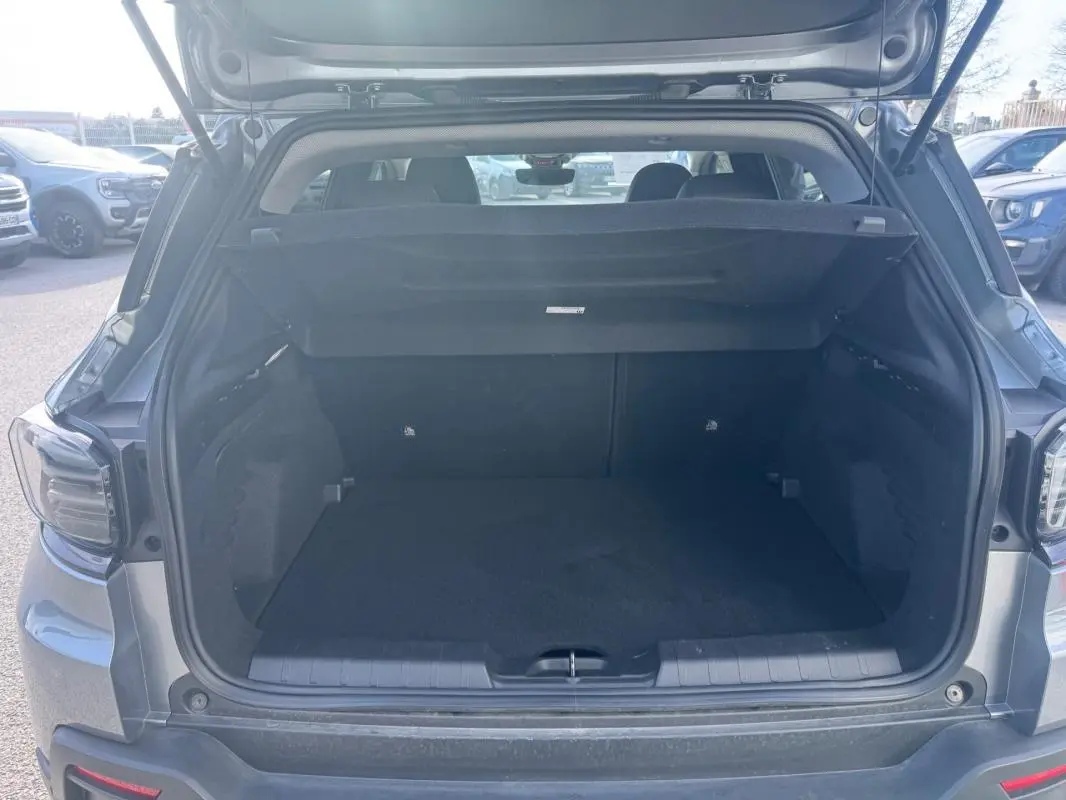 Coffre ouvert d’un Jeep Avenger gris 2025, vue arrière montrant l’espace de chargement vide et la plage arrière relevée.