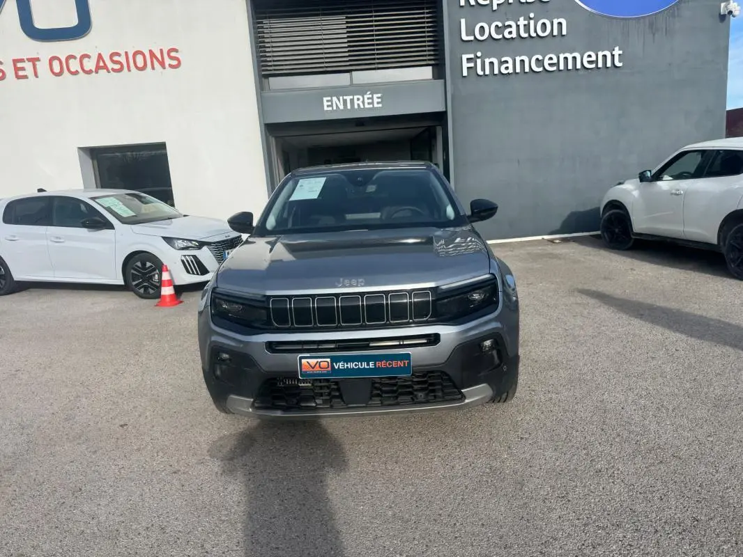 Vue avant d'un Jeep Avenger gris 2025 garé devant un bâtiment avec plaque V.O. Véhicule récent.