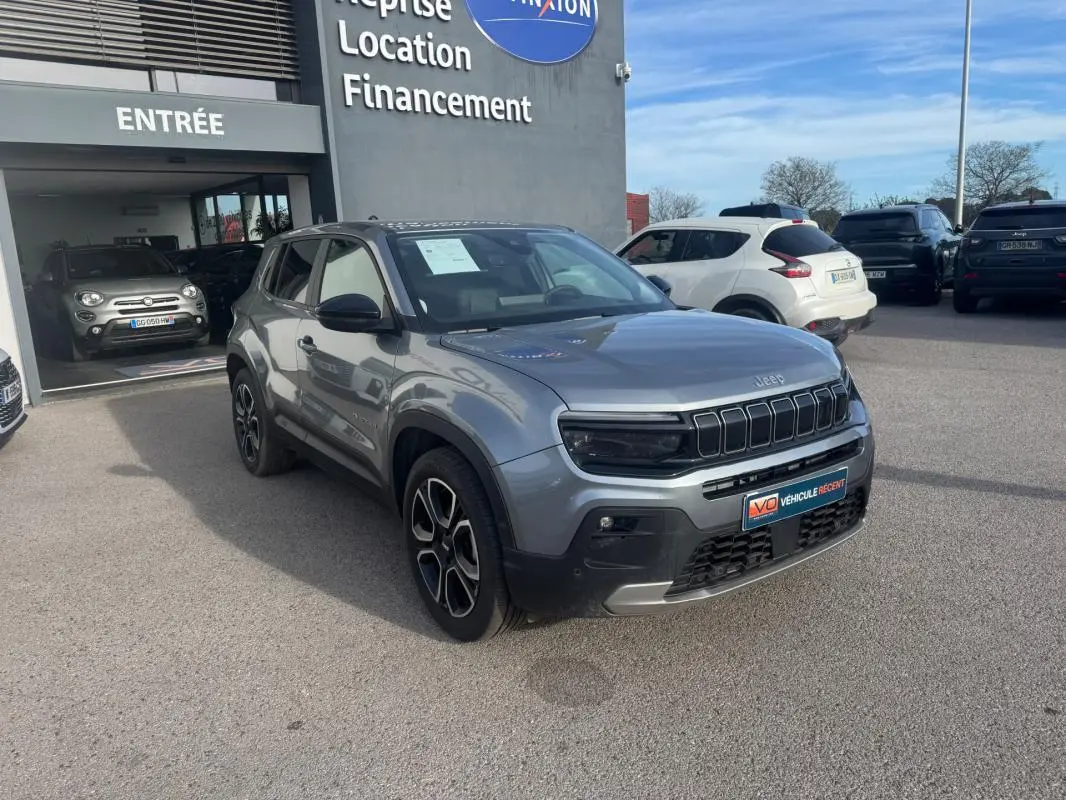 Jeep Avenger gris 3/4 avant droit, SUV compact avec calandre noire distinctive, stationné devant un concessionnaire.