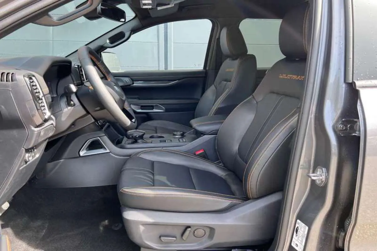 Vue intérieure côté conducteur du Ford Ranger Wildtrak Plus 2025, sièges cuir noirs avec surpiqûres orange et volant multifonctions.
