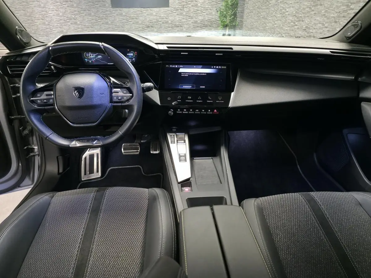 Vue intérieure avant de la Peugeot 308 GT 2024, tableau de bord noir avec écran tactile central et volant cuir.