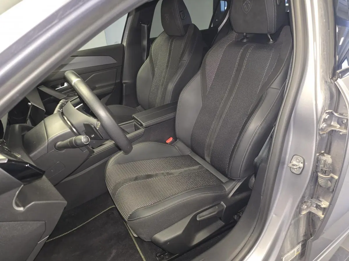 Vue intérieure côté conducteur de la Peugeot 308 gris 2024, sièges sport en tissu et cuir avec logo Peugeot brodé.
