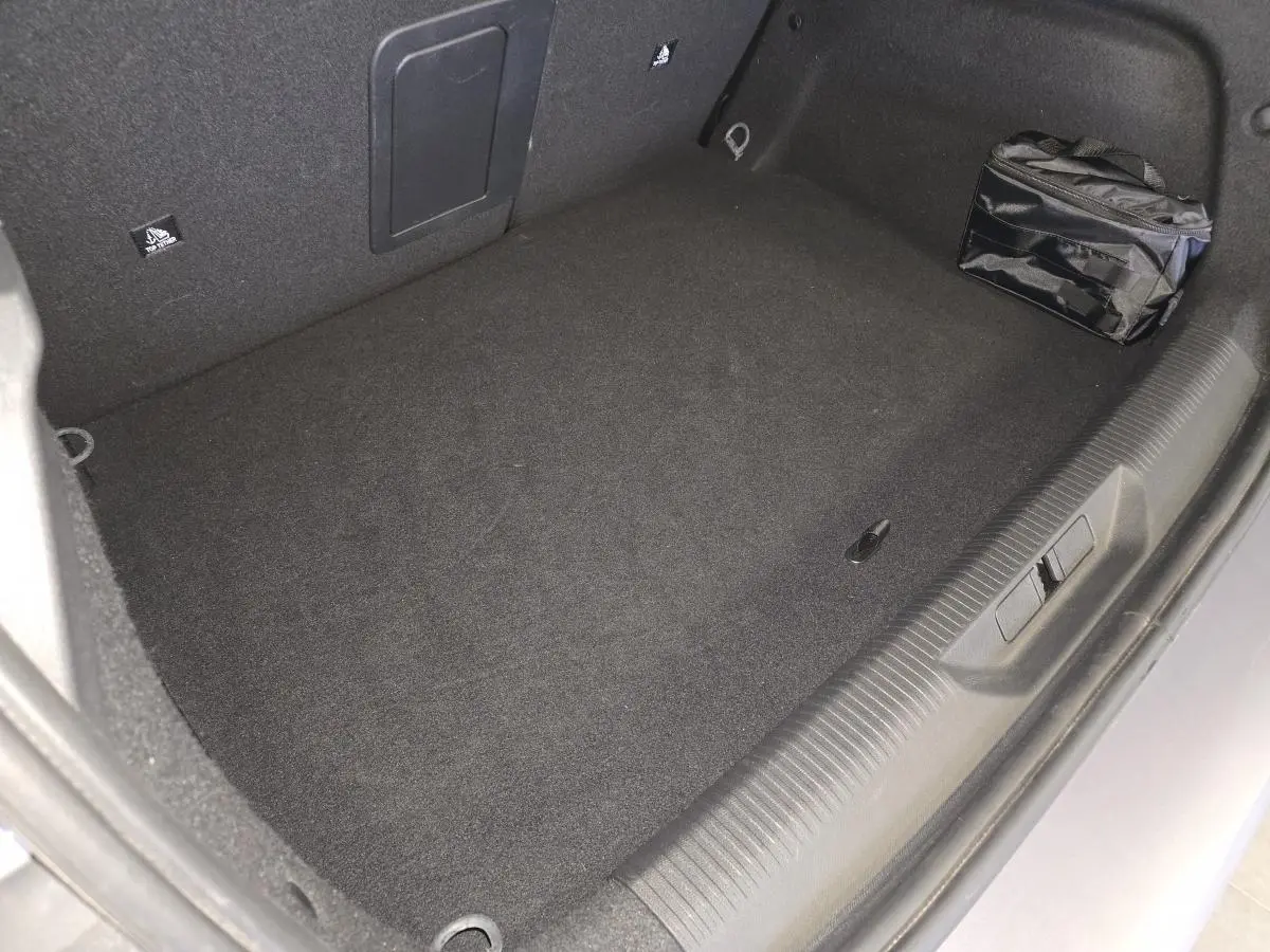 Vue intérieure du coffre gris du Peugeot 308 1.6 PHEV 2024 avec sac de rangement noir sur le côté droit.