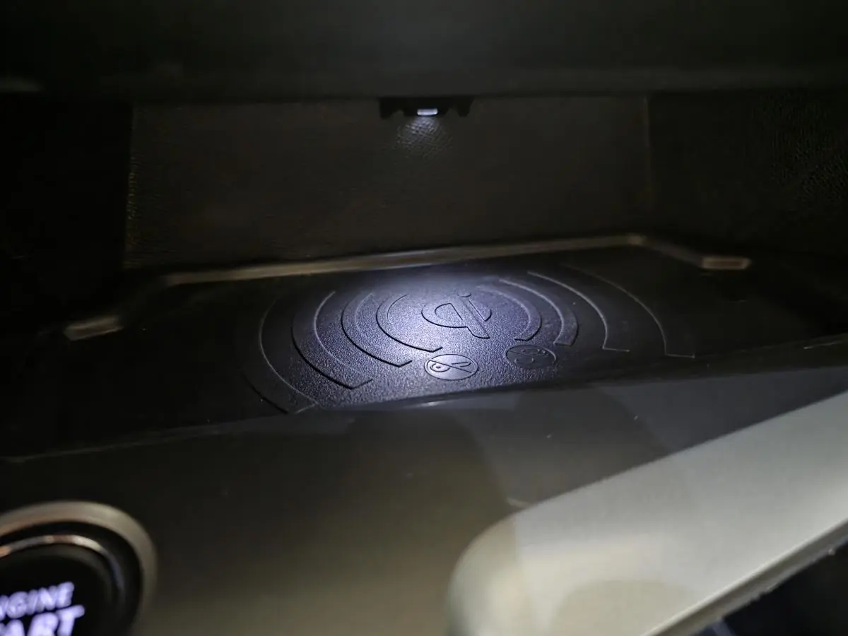Gros plan sur le chargeur à induction noir dans l'habitacle de la Peugeot 308 gris 2024, éclairé par une LED.