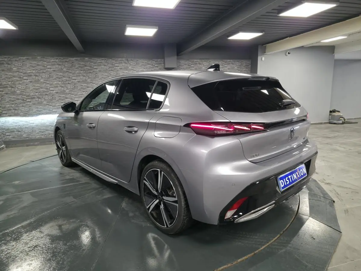 Vue 3/4 arrière gauche d'une Peugeot 308 gris métallisé 2024 avec feux arrière LED et jantes alliage 18 pouces.