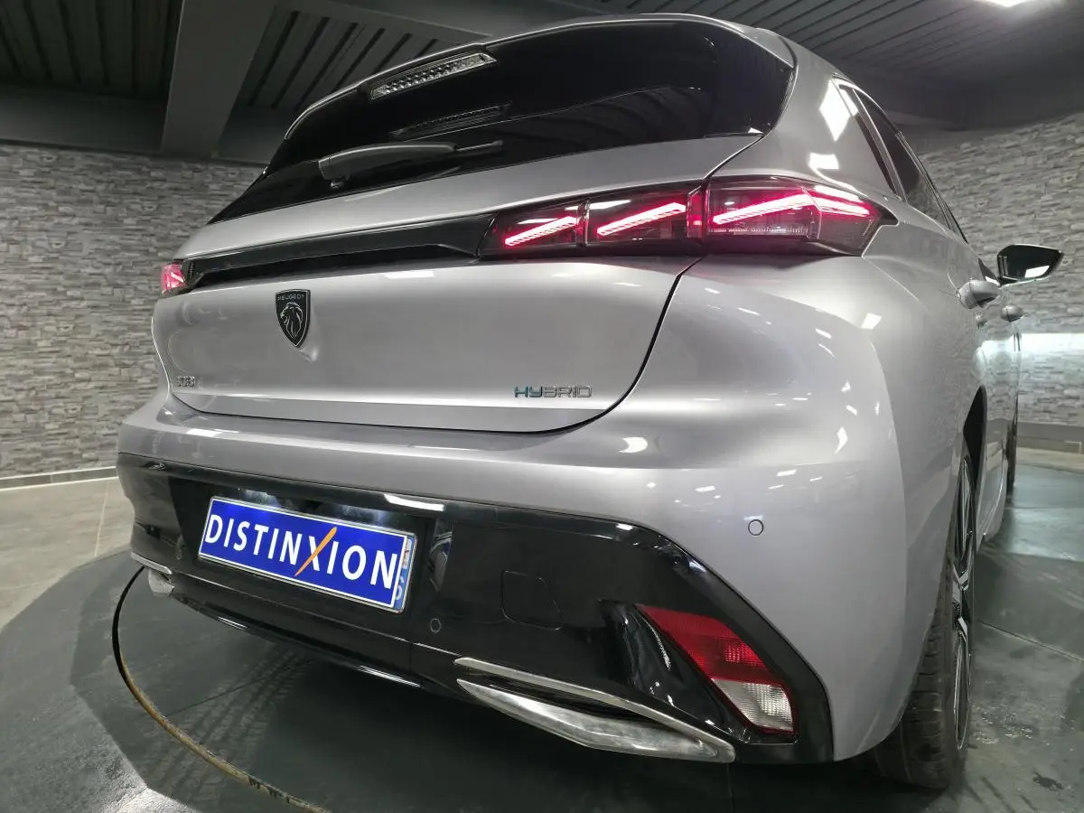 Vue 3/4 arrière droite d'une Peugeot 308 hybride rechargeable gris métallisé avec feux arrière LED griffés et diffuseur noir brillant.