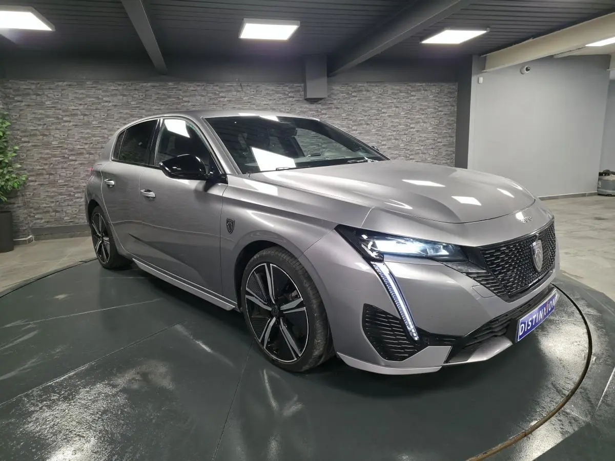 Peugeot 308 gris métallisé vue 3/4 avant droit avec calandre noire brillante et feux LED griffés.