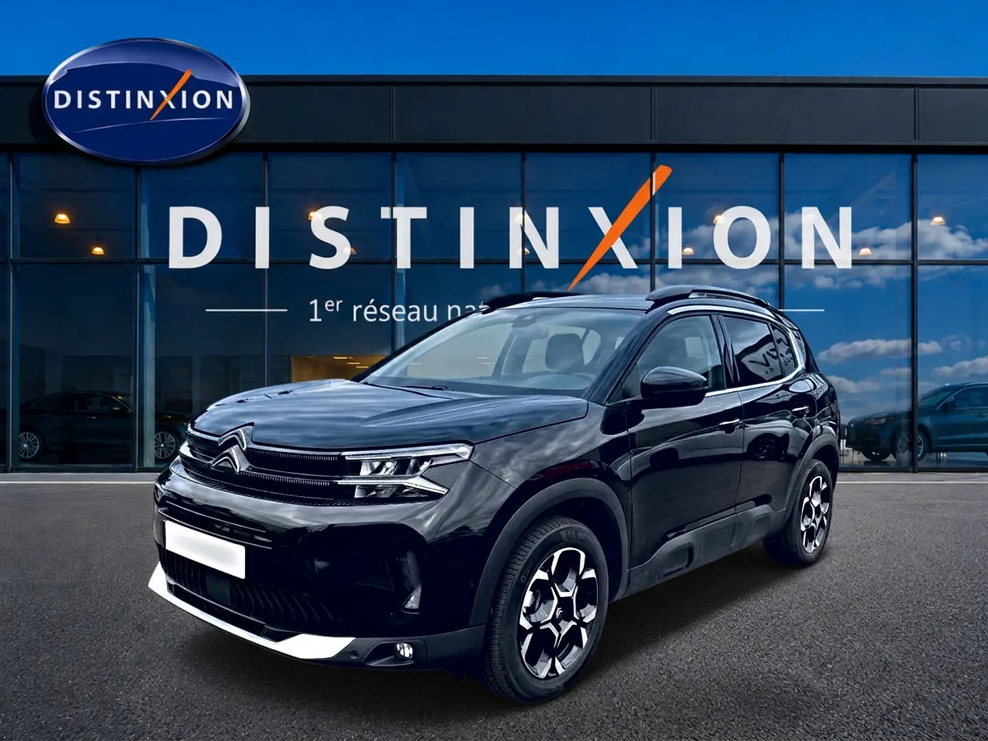 Citroën C5 Aircross noir vue 3/4 avant droit, avec jantes alu et barres de toit visibles devant une vitrine Distinxion.
