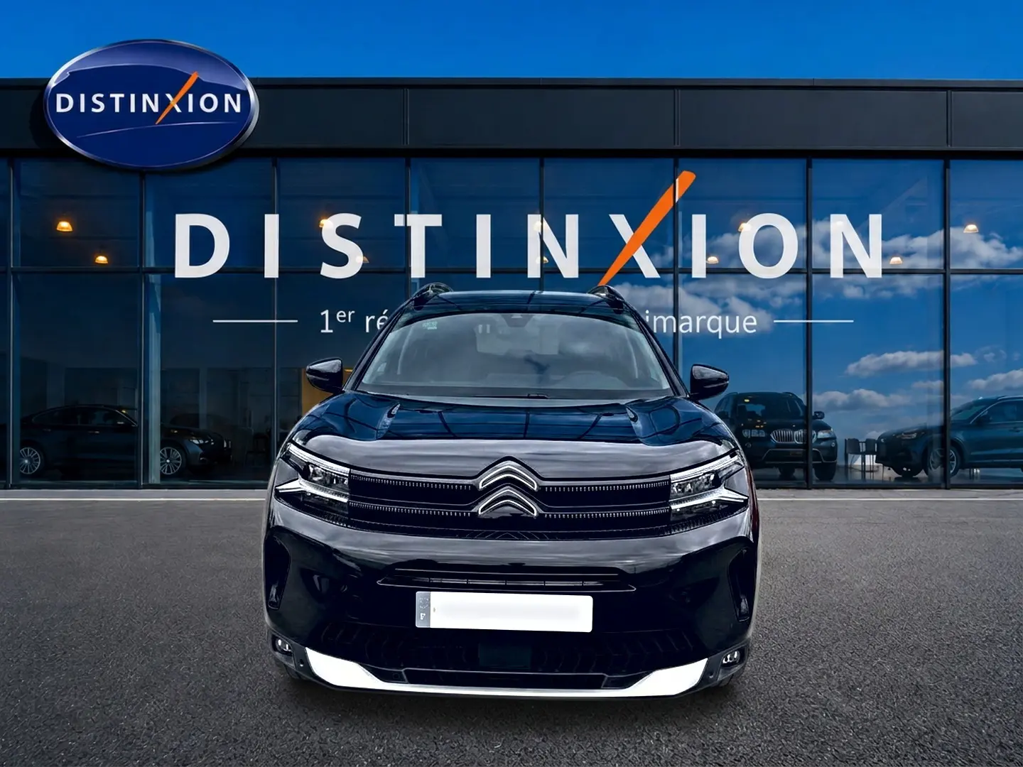 Vue frontale d'un Citroën C5 Aircross noir 2025 avec calandre distinctive et barres de toit visibles devant une vitrine.
