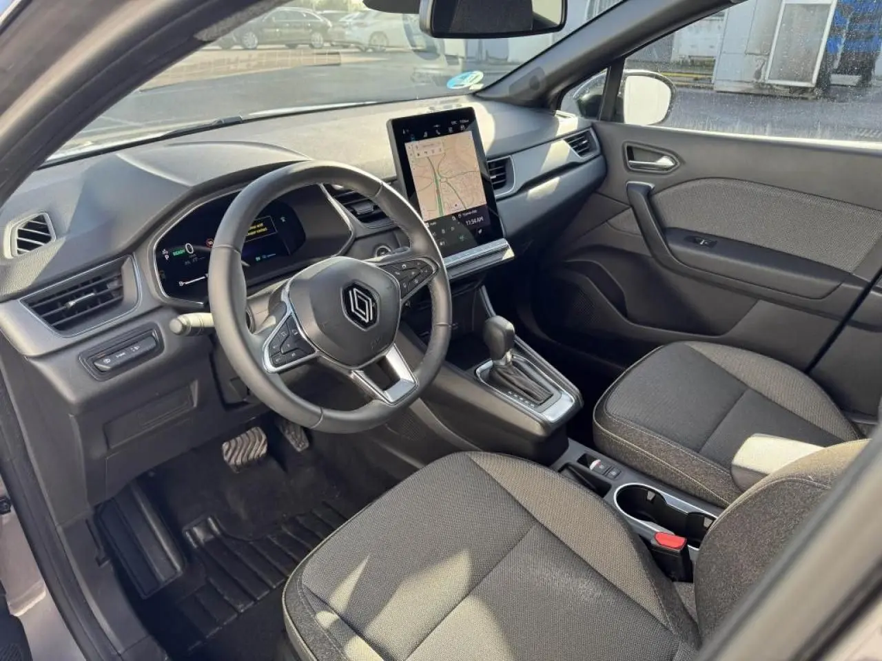 Vue intérieure côté conducteur du Renault Captur II gris Cassiopée, volant multifonction et écran tactile vertical avec navigation affichée.