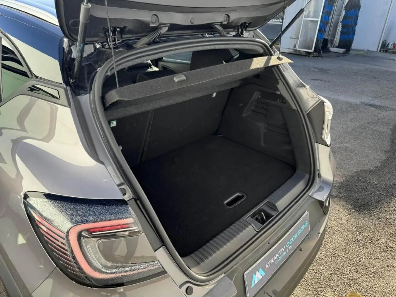 Coffre ouvert vu en 3/4 arrière droit d’un Renault Captur gris Cassiopée avec toit noir, montrant l’espace de chargement.