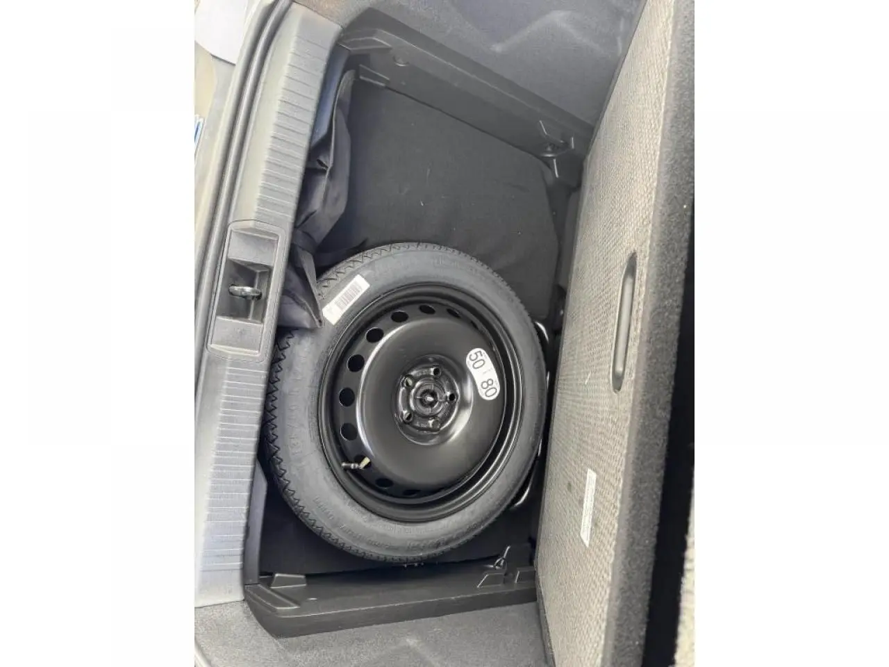 Vue plongeante sur la roue de secours noire dans le coffre du Renault Captur gris Cassiopée toit noir.