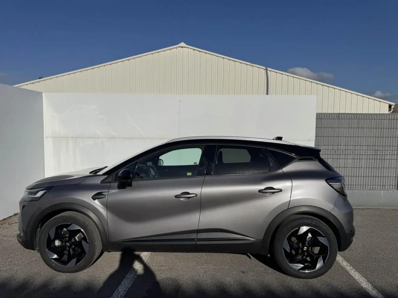 Profil droit du Renault Captur gris Cassiopée avec toit noir, jantes noires et lignes modernes visibles au soleil.
