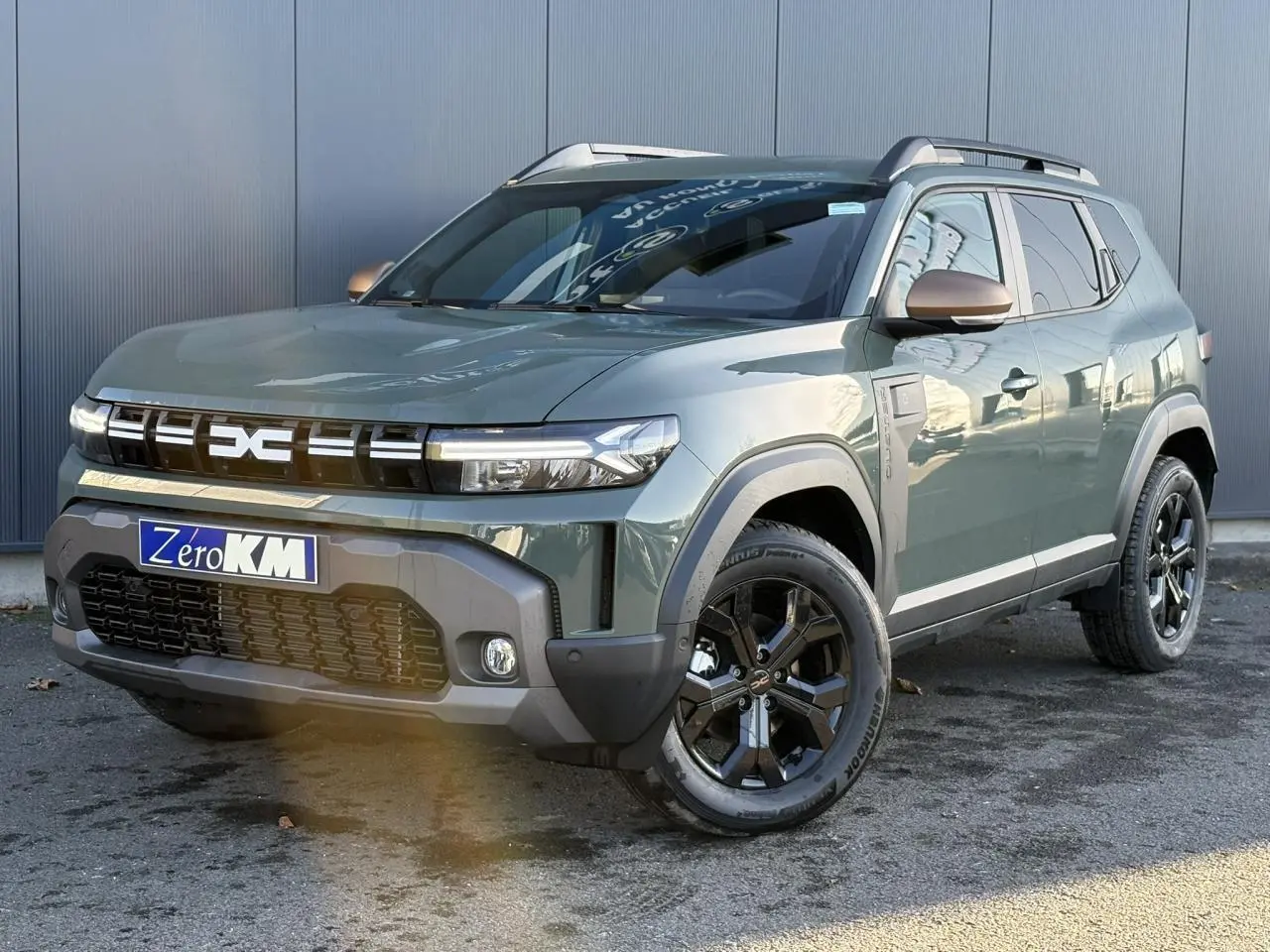 SUV Dacia Duster 2025 Kaki Lichen en 3/4 avant droit avec jantes noires et barres de toit argentées.