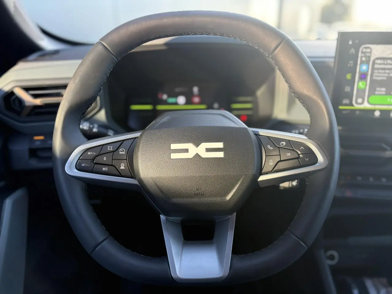 Vue rapprochée du volant noir du Dacia Duster 2025 avec commandes intégrées et tableau de bord digital en arrière-plan.