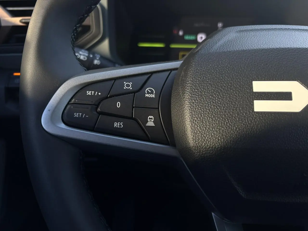 Gros plan sur le côté gauche du volant noir du Dacia Duster 2025, avec commandes de régulateur de vitesse et finition argentée.