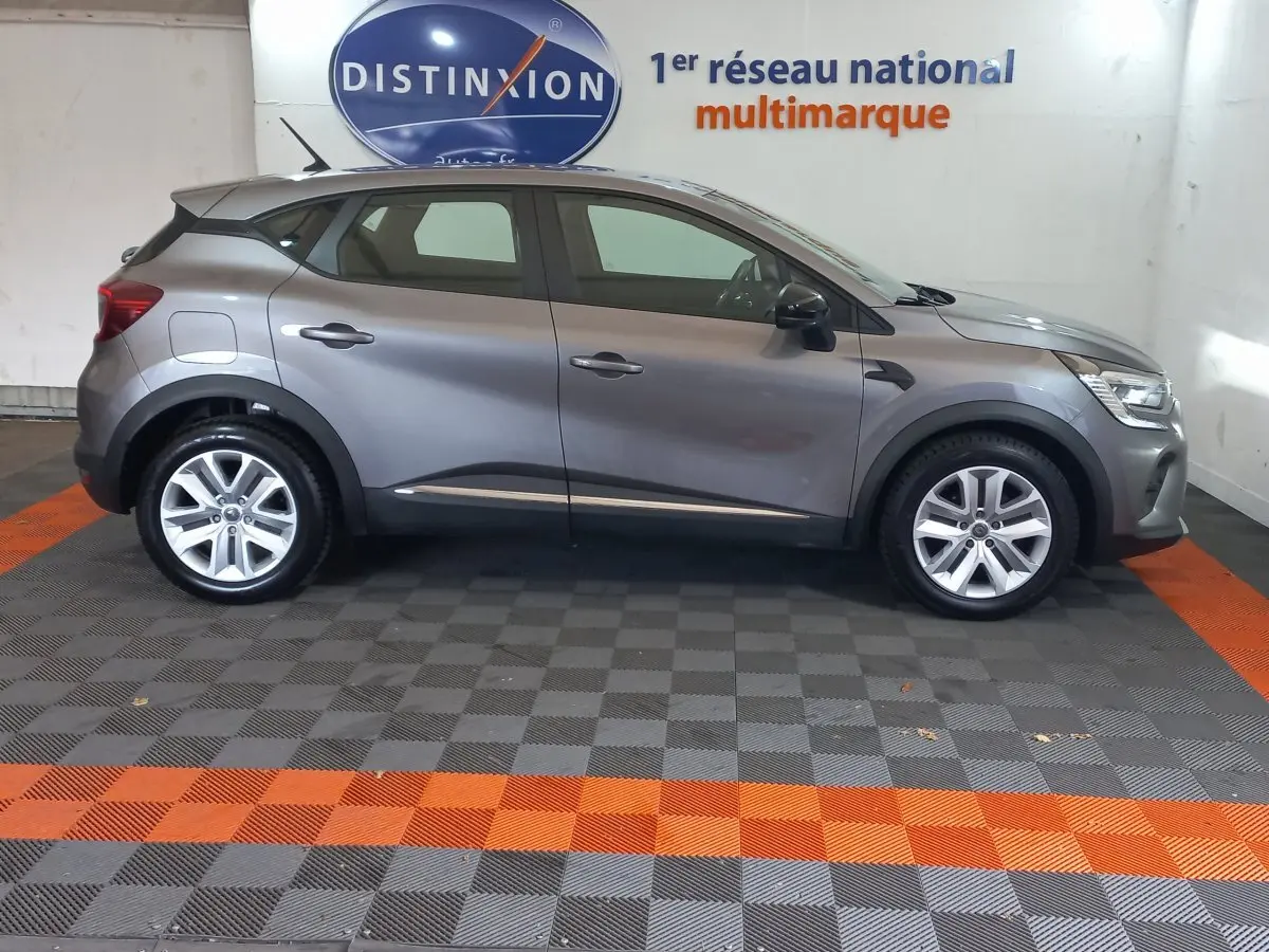 Profil droit d'un Renault Captur Business TCe 100 gris clair stationné en intérieur sur un sol damier gris et orange.
