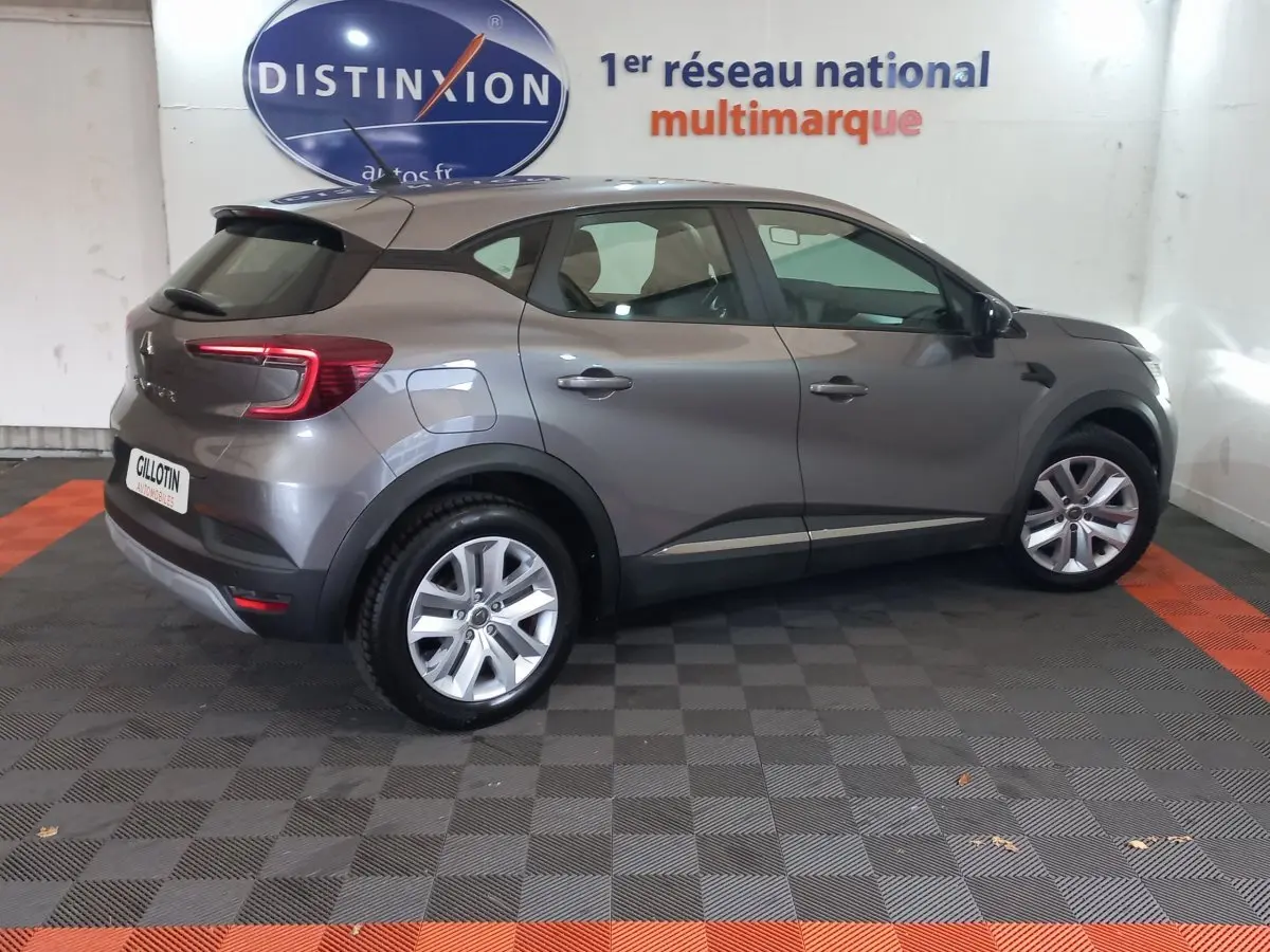 Renault Captur Business gris clair vu de profil côté droit, stationné en intérieur avec logo Distinxion en arrière-plan.