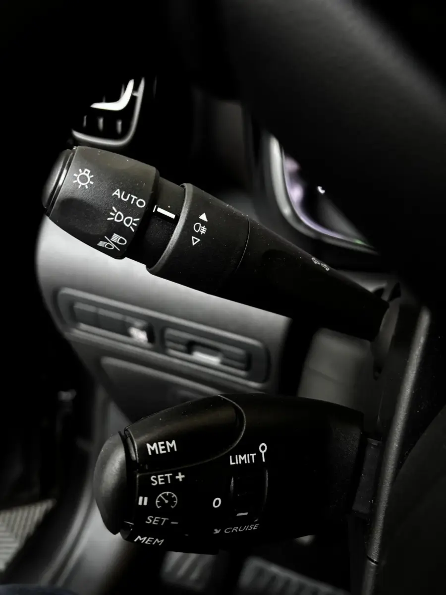 Gros plan sur les commandes au volant noir du Citroën C3 Aircross 2024, avec réglages feux et régulateur de vitesse.