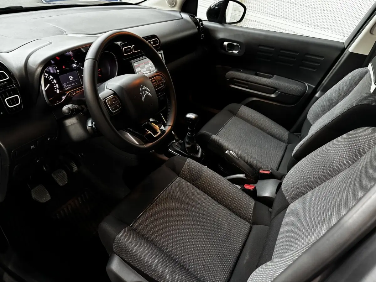 Intérieur avant droit du Citroën C3 Aircross 2024, sièges tissu gris, volant cuir multifonctions et tableau de bord noir.
