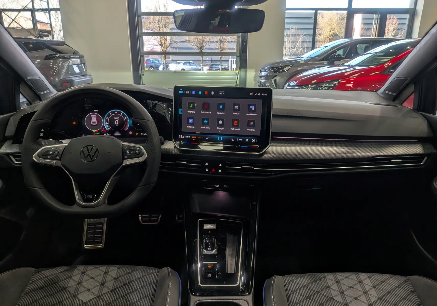 Vue intérieure frontale du tableau de bord de la Volkswagen Golf 1.5 eTSI gris dauphin avec écran tactile central et volant multifonction.