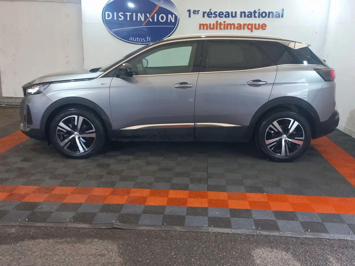 Vue latérale droite d'un Peugeot 3008 gris clair 2022 avec toit noir et jantes alliage bicolores, en intérieur showroom.