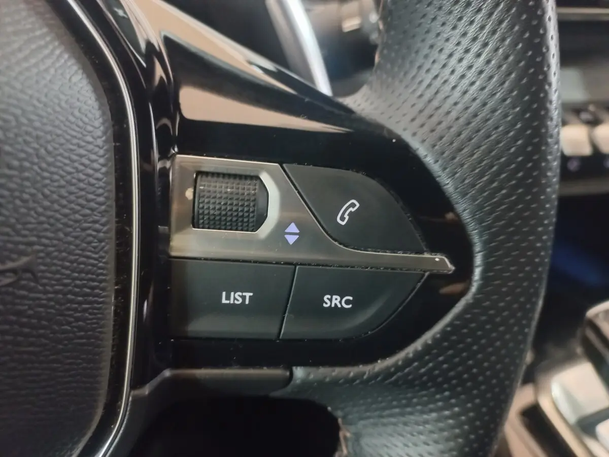 Gros plan sur les commandes gauche du volant cuir perforé du Peugeot 3008 gris clair, boutons LIST et SRC visibles.